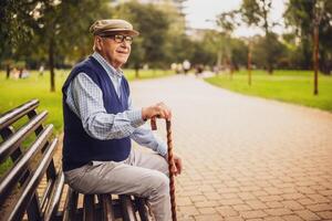 Portrait of happy senior man in park. He is sitting on bench and enjoying autumn day. photo