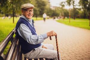 Portrait of happy senior man in park. He is sitting on bench and enjoying autumn day. photo