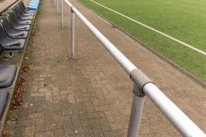 Empty bench and metal railing overlooking artificial turf soccer field photo