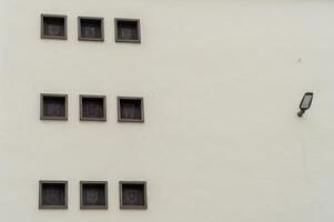 White wall showing nine square windows with a lamp on the right side photo