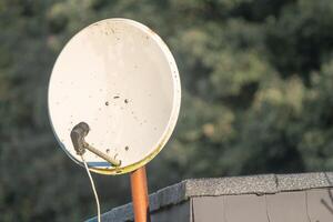 Satellite dish on a roof capturing signals with blurred trees in background photo