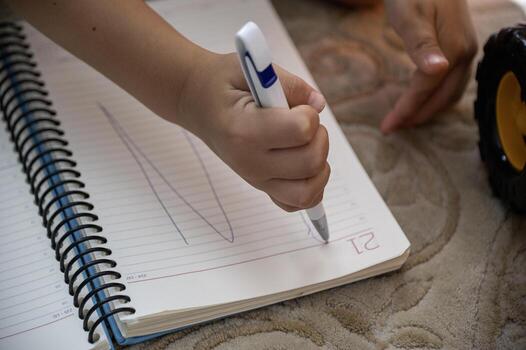The child learns to write. the pen in his hands and he writes on a notebook.The child's hand with pencil photo