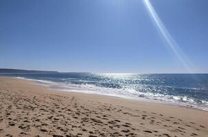 A serene beach at midday with gentle waves lapping the shore and clear blue skies inviting relaxation photo