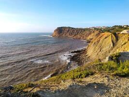 Coastal cliff view of rough waves crashing against the rocks in the afternoon sunlight at a scenic seaside location photo