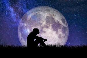 Silhouette of a Person Sitting in Front of a Large Full Moon with a Starry Night Sky Background photo