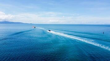 Aerial View of Boats Creating Wake Trails on Vibrant Blue Ocean Under Clear Sky on a Sunny Day photo