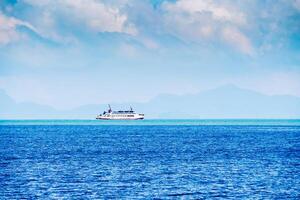 Scenic View of a Ferry Sailing Across the Calm Blue Ocean with Mountains in the Background Under a Cloudy Sky photo