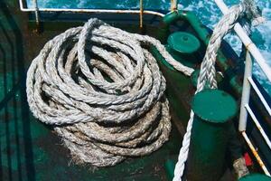 Close-Up of Coiled Rope on a Weathered Ship Deck with Ocean Waves in the Background photo