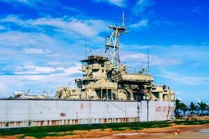 Abandoned Military Ship on Shoreline Under Blue Sky with Clouds and Palm Trees in Background photo