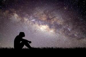 Silhouette of a Person Sitting Under a Starry Night Sky with the Milky Way in the Background photo