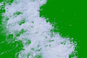 Dynamic Ocean Wave Splashing Against Vibrant Green Background Captured in Motion photo