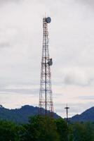 Tall Communication Tower Against a Cloudy Sky with Lush Greenery and Distant Hills in the Background photo