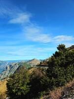 Vertical view of the mountainous landscape near the Bay of Kotor, Montenegro, with green trees, a winding road, and a bright blue sky with copy space. Ideal for travel ads, posters, or social media photo