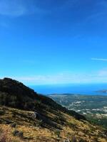 Vertical view of a grassy mountain slope with distant views of the coastline and the Adriatic Sea near the Bay of Kotor, Montenegro, under a clear blue sky. Perfect for nature or travel brochures. photo