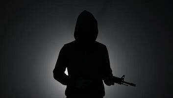 Silhouette of a hooded figure with a gun exuding mystery and danger photo