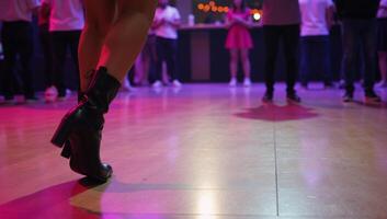 A vibrant dancefloor scene features a dancer wearing black boots grooving away photo