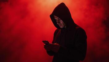 Hooded figure gazing into phone amidst swirling red mist photo