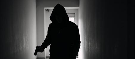Silhouette of a hooded figure with a gun exuding mystery and danger photo