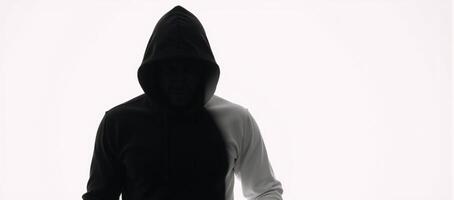 Dark isolated portrait of a hooded hacker in a black silhouette against a stark white backdrop photo