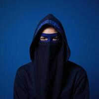Veiled figure with blue mask and hood against a blue backdrop Mystery photo