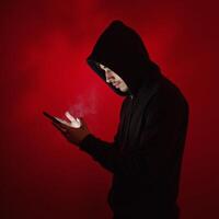 Hooded figure gazing into phone amidst swirling red mist photo