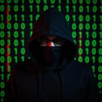 Hooded hacker in front of binary code backdrop photo