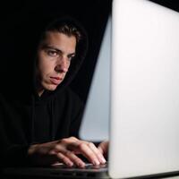 A hacker engages in cybercrime through his laptop on a dark backdrop while a young hacking prodigy battles him in an Internet Security Standoff photo
