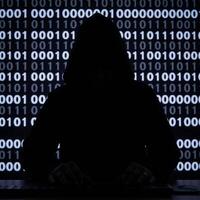 A hooded criminal silhouetted while hacking on binary code background cybercrime concept photo