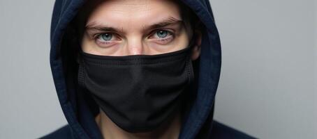 Masked man in dark hoodie with piercing blue gaze photo