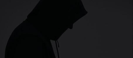 Man silhouetted with hood on dark backdrop anonymous figure in hoodie photo