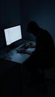 Hacking computer in dim room hooded cybercriminal using malware for device intrusion photo