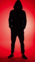 Man in hood with no visible face silhouetted against red background photo