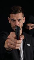Attacker brandishing weapon gun targets individual donning black mask and hoodie in threatening scenario photo