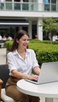 A laughing businesswoman is depicted working on her laptop amidst an office park setting photo