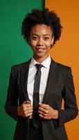 A young businesswoman sporting an afro and dressed in office attire stands amidst a vibrant mix of warm oranges and cool greens photo