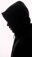 Dark isolated portrait of a hooded hacker in a black silhouette against a stark white backdrop photo
