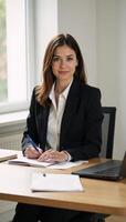 Businesswoman portrayed professionally in casual pose at her desk under natural window light in corporate setting photo
