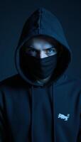 A darkhoodied masked man with piercing blue eyes looks straight into the camera photo