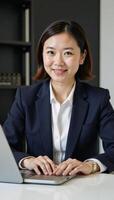 Asian woman with short hair and office suit poses while holding laptop photo