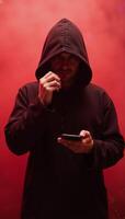 Hooded figure in red mist focused on smartphone photo