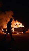 Hooded figure passing by flaming wreckage at twilight photo