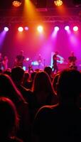 A lively concert scene featuring an enthusiastic crowd raising their arms amidst vibrant stage lighting as the band performs live photo