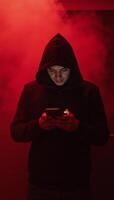 Hooded figure gazing into phone amidst swirling red mist photo