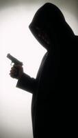 Hooded figure with gun in dark silhouette photo