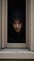 A mysterious hooded figure gazes intently from behind a window photo