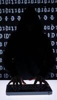 A hooded criminal silhouetted while hacking on binary code background cybercrime concept photo