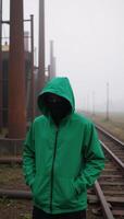 Person in a green hooded jacket amidst an industrial misty environment photo