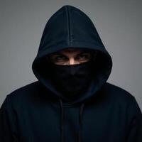 A darkhoodied masked man with piercing blue eyes looks straight into the camera photo