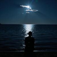 Lone figure contemplates under moonlit sky by waters edge photo