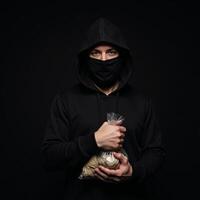 A shadowy bank robber stands against a dark backdrop clutching a bag of stolen cash outlined by a hint of a closed bank door photo